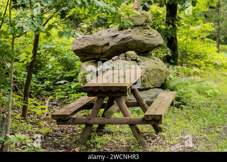 Table de pique-nique en bois dans le parc public avec des débris sur le dessus assis devant de grandes pierres Banque D'Images