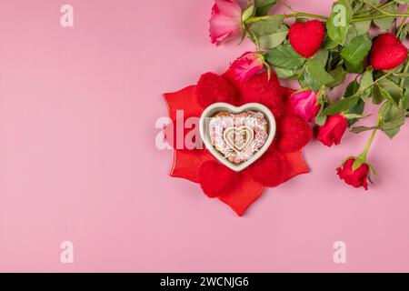 Bouquet de roses à côté d'un bol en forme de coeur avec un muffin entouré de coeurs rouges sur un fond rose Banque D'Images