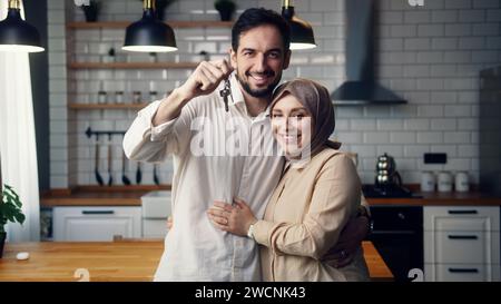 Jeune couple nouvellement marié debout dans le sourire de cuisine regarder le mari de la caméra montrer un tas de clés de la nouvelle maison. Fiers propriétaires, appartement loué, prêt mor Banque D'Images