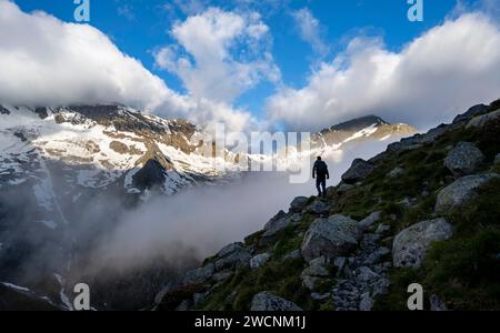 Silhouette d'un alpiniste devant un paysage montagneux nuageux et atmosphérique, des montagnes rocheuses couvertes de neige avec le sommet Hochsteller Banque D'Images