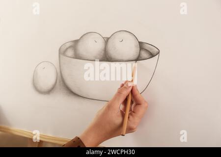 Femme dessinant un bol de fruits avec un crayon graphite sur toile, closeup Banque D'Images