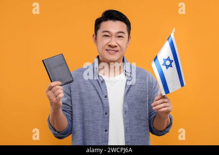 Immigration. Homme heureux avec passeport et drapeau d'Israël sur fond orange Banque D'Images