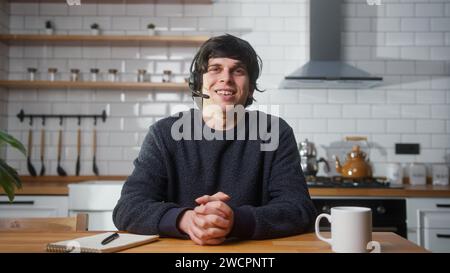 Jeune homme porte un casque sans fil avec microphone parlant à la caméra faisant la conduite d'une conférence téléphonique d'affaires dans la cuisine. Avoir un appel vidéo zoom meeti Banque D'Images