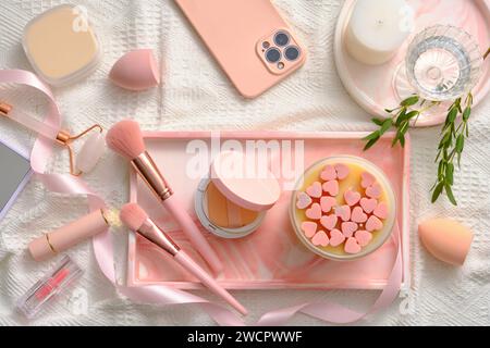 Joli concept rose avec un plateau rectangulaire présentant une bougie parfumée, un coussin compact, des pinceaux de maquillage et d'autres produits de maquillage affichés. Produits de maquillage Banque D'Images