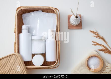 Bougie parfumée, bouteilles de pompe, draps de masque et un pot de gommage présentés dans un panier en bambou. Diffuseurs de roseau et un bol de gommage au sel en vedette. Maquette de Banque D'Images