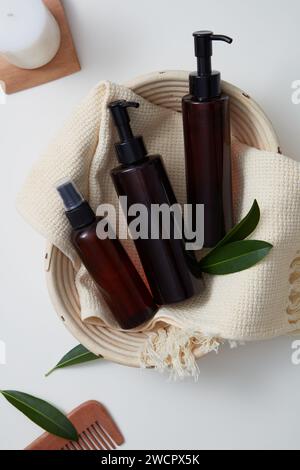 Un panier comportait une écharpe en laine blanche avec flacon pulvérisateur et bouteilles à pompe sans étiquette. Peigne en bois et bougie parfumée disposés à côté avec feuille verte Banque D'Images