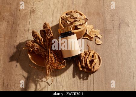 Racine d'angélique placée sur des assiettes en bois et un bol en bois de Bai Zhu arrangé avec un pot en verre non étiqueté de médecine. Maquette de médecine traditionnelle br Banque D'Images