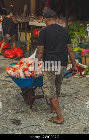 Balikpapan, Indonésie - 11 janvier 2024. Un homme livre un chariot plein de viande de poulet au vendeur du marché. Banque D'Images