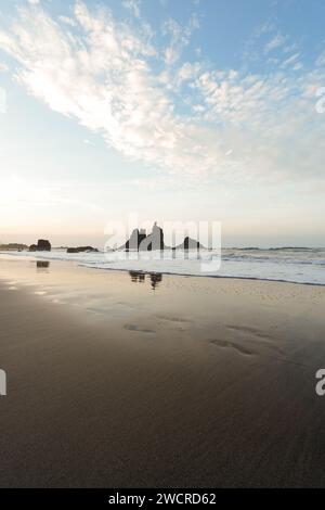 Une plage sereine à l'heure d'or, où roche, eau, sable et ciel s'unissent en harmonie, capturés dans un cadre vertical Banque D'Images