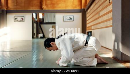 Homme asiatique, classe et arc dans le dojo pour le respect, le salut ou l'honneur à maîtriser à la salle de gym intérieure. Personne masculine ou groupe en karaté s'inclinant sur le sol pour l'étiquette Banque D'Images