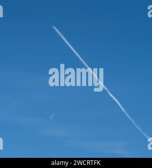 Un avion survolant le ciel bleu clair, laissant derrière lui de longs contrails blancs dans leur sillage Banque D'Images