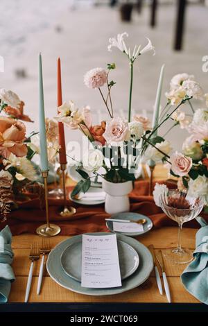 Le menu festif se trouve sur une assiette à côté de l'invitation sur une soucoupe devant un bouquet de fleurs sur la table Banque D'Images