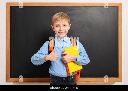 Heureux écolier avec sac à dos et livres près du tableau noir Banque D'Images