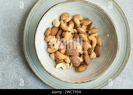 Un mélange d'amandes, de noix de cajou et d'autres noix présenté dans un bol en céramique rustique sur une surface grise texturée Banque D'Images