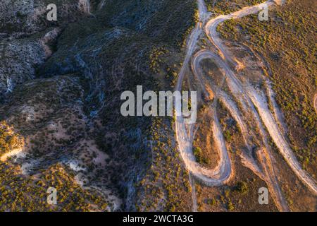 La lumière du coucher du soleil projette des ombres sur un chemin de terre sinueux serpentant à travers le terrain vallonné d'Alcarria Banque D'Images