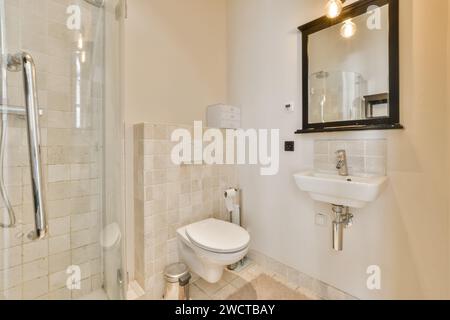 Une vue intérieure d'une salle de bains propre et aux tons neutres avec douche en verre, toilettes et lavabo, avec éclairage moderne. Banque D'Images
