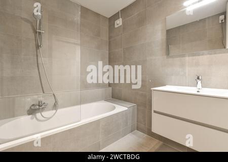 Salle de bains moderne et épurée avec baignoire et douche combinées, carrelage beige élégant et meubles minimalistes. Banque D'Images