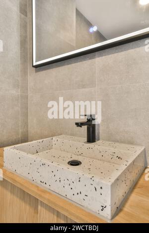 Lavabo contemporain en terrazzo, avec luminaires noirs et vanité en bois, éclairé par un grand miroir avec éclairage LED. Banque D'Images