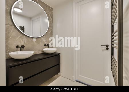 Salle de bains contemporaine avec grand miroir, deux lavabos sur une élégante coiffeuse et chauffe-serviettes. Banque D'Images