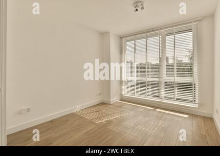 Une pièce vide avec la lumière du soleil qui brille à travers une grande fenêtre avec des stores vénitiens sur un plancher en bois, créant un espace chaleureux et accueillant. Banque D'Images