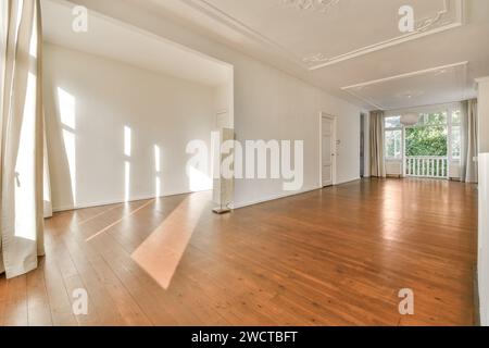 Une pièce vide et lumineuse avec parquet poli, grandes fenêtres, murs blancs et détails élégants du plafond. Banque D'Images