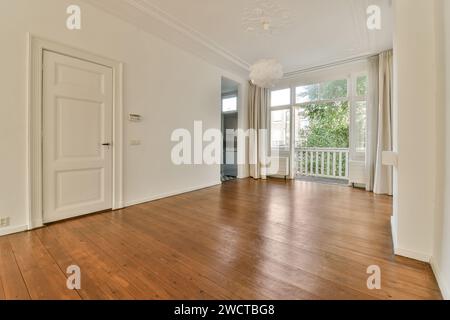 Une pièce vide avec des planchers de bois franc poli, des murs blancs et de grandes fenêtres avec des rideaux clairs. L'espace est orné d'un simple plafonnier A. Banque D'Images