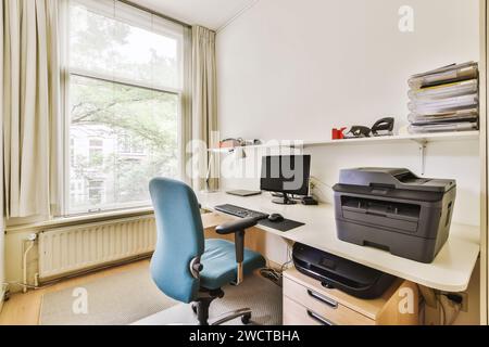 Bureau à domicile lumineux avec un espace de travail bien rangé avec un ordinateur, une chaise ergonomique, une imprimante et des étagères organisées près d'une grande fenêtre. Banque D'Images