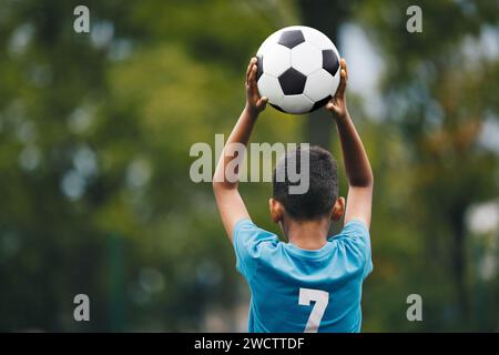 Football jeter dans pendant le jeu de sport pour enfants. Petit garçon tenant le ballon de football dans les mains. Enfants jouant dans football League. Garçon en maillot bleu de football avec Banque D'Images