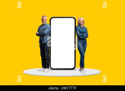 Adultes matures avec écran géant de smartphone, fond jaune Banque D'Images