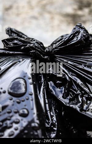 GOIANIA GOIAS BRÉSIL - 14 JANVIER 2024 : détail d'un noeud dans un sac en plastique noir avec des ordures, mouillé, avec des gouttes d'eau de pluie. Banque D'Images