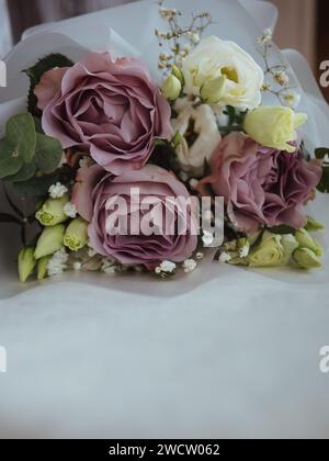 Gros plan vertical d'un bouquet de roses violettes et blanches, d'eucalyptus et de gypsophila blanche sur une surface blanche. Banque D'Images