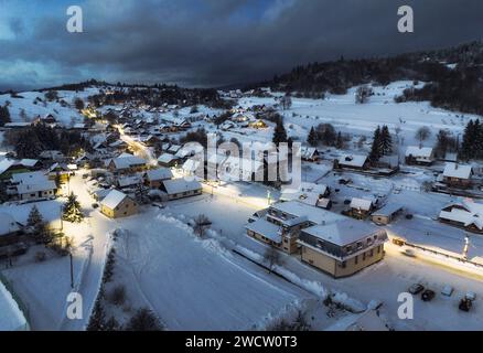Vue sur la chaîne de montagnes enneigées et le village avec des maisons illuminées situées au bas de la colline en Slovaquie au coucher du soleil Banque D'Images