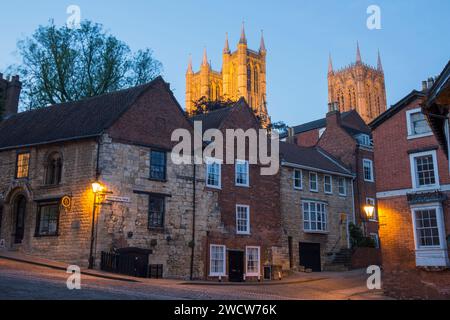 Lincoln, Lincolnshire, Angleterre. Vue sur la colline pavée de Steep Hill jusqu'aux tours illuminées de la cathédrale de Lincoln, au crépuscule. Banque D'Images