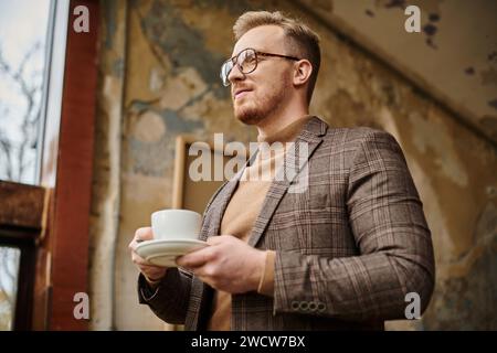 joyeux chef d'entreprise sophistiqué avec des lunettes en costume élégant buvant son café chaud Banque D'Images