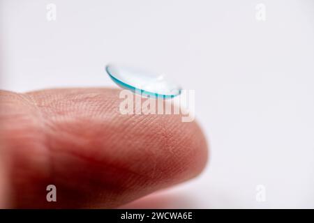 Vue latérale macro d'une lentille de contact oculaire sur le bout d'un doigt isolé sur un fond blanc. Banque D'Images