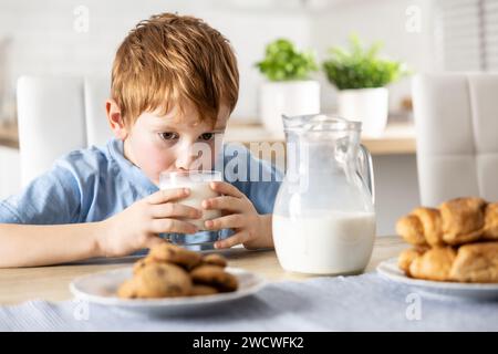 Mignon garçon boit du lait frais pour le petit déjeuner. Banque D'Images