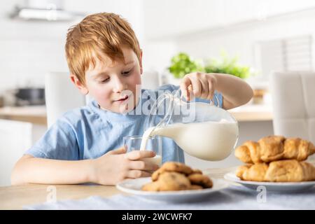 Un petit garçon se verse du lait frais pendant le petit déjeuner. Banque D'Images