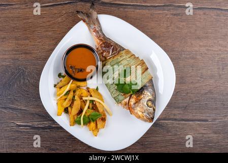 Vue de dessus du poisson dorado cuit au four et des pommes de terre avec des pousses de bambou et sauce Sichuan sur une assiette blanche. Cuisine maison. Banque D'Images