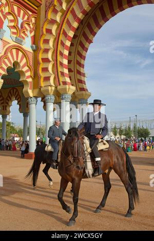 Espagne, Andalousie, Cordoue, cavaliers en costume traditionnel à cheval devant la porte d'entrée monumentale jaune et rouge de la feria de Nuestra Señora de la salud Banque D'Images
