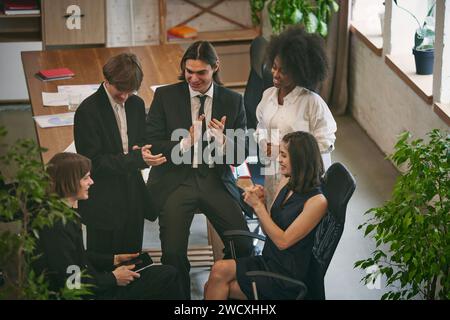 Vue aérienne. Étudiants universitaires étudiant ensemble à table et un homme parlant, lisant des informations pour leur projet. Banque D'Images