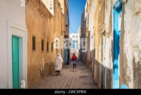 Une femme tunisienne âgée vêtue d'un foutah traditionnel et une jeune femme moderne descendent une ruelle dans l'ancienne médina de Kairouan en Tunisie. KAIR Banque D'Images