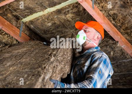 un travailleur en salopette, gants et respirateur tient une tasse avec du coton à la main. Il est en cours de préparation pour le placement sur le plafond. Banque D'Images