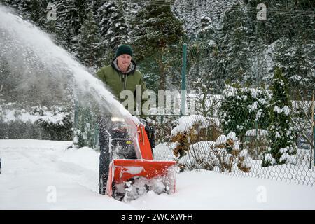 l'homme pelle la neige avec une souffleuse à neige rouge, éclaboussures de neige sur le côté - vue rapprochée. Banque D'Images