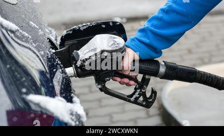 un gars dans un sweat à capuche bleu tient un pistolet à carburant - ravitailler une voiture gelée en hiver et un arrière-plan flou. Banque D'Images