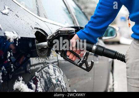 un gars dans un sweat à capuche bleu tient un pistolet à carburant - ravitailler une voiture gelée en hiver et un arrière-plan flou. Banque D'Images