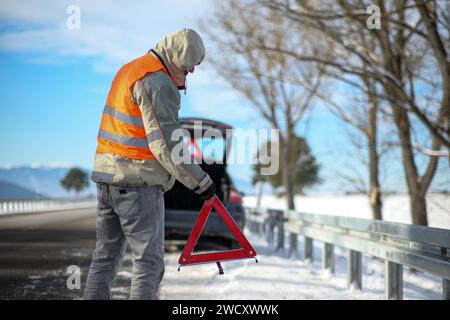 le conducteur d'un véhicule à moteur a eu une panne de voiture en conduisant sur la route en hiver, il a mis un triangle de signalisation sur la route. gros plan et bl Banque D'Images