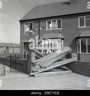 Années 1960, historique, juste marié.... sur un nouveau lotissement, planches de construction en bois barricadant l'allée d'une maison récemment construite décorée avec des banderoles et des avis de mariage amusants, slogans nouvellement mariés incluent, pas d'appelants après 18h30, cabane de snoggers - leçons!, New Weds - Do Not Disturb, conseillez Wanted! Banque D'Images