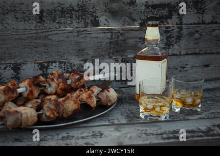 une bouteille de whisky et une assiette de porc frit sur des brochettes, versé dans deux verres, situés à l'air libre Banque D'Images