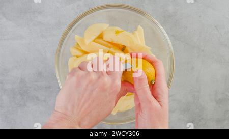 Les mains de la femme zestent le citron à l'aide d'un zester d'agrumes, en tapissant les tranches de pomme avec le jus de citron et le zeste de citron. Recette de gâteau aux pommes Banque D'Images