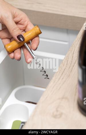 femme tient un tire-bouchon dans sa main pour ouvrir une bouteille de vin. la main d'une femme prend un tire-bouchon dans un tiroir de cuisine. alcoolisme féminin. photophot vertical Banque D'Images